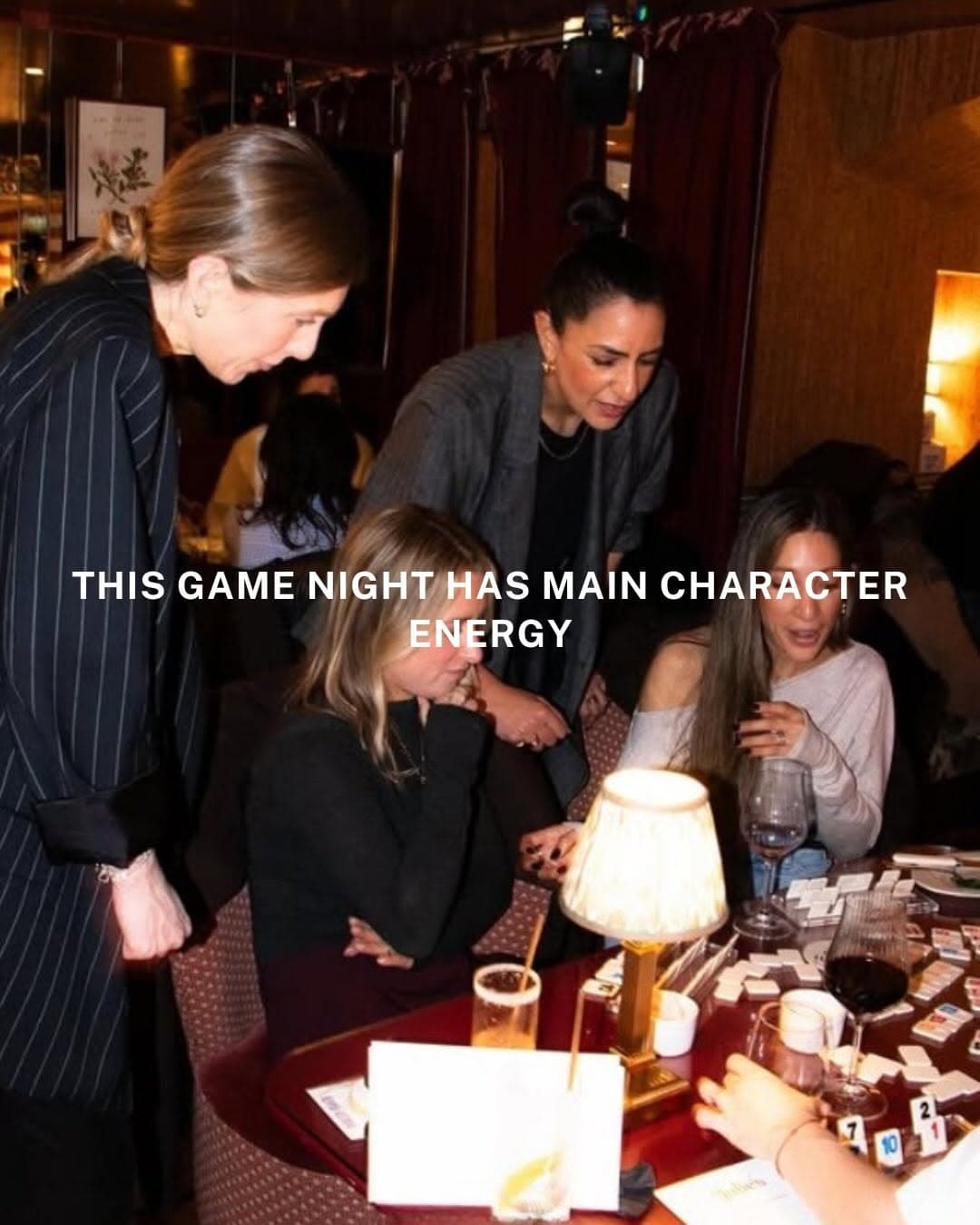People gathered around tables playing Rummikub board game at RummiKlubLA community event with warm lighting and social atmosphere